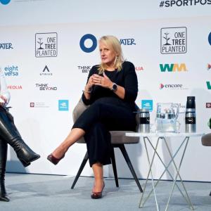 Three people seated on a stage, a table with drinks on it between them