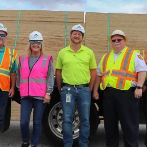 Five people in hard hats and high-vis vests in front of a trailer loaded with OSB boards.