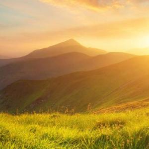 A sunset over mountain range with grassy plains.