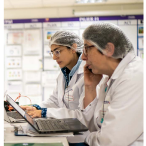 Two people working next to each other on laptops, wearing protective lab gear.