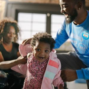 people helping a child put on a coat