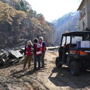 Three workers talking together next to a river, and a vehicle loaded with supplies