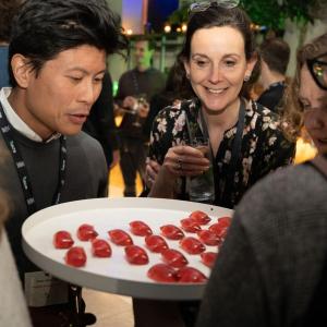 Two attendees looking over a platter of bright red edible cocktails