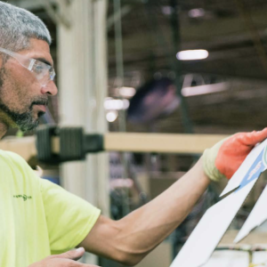 worker in a yellow shirt and orange gloves inspecting a piece of cardboard