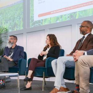 Panel of five seated on a stage, one speaking to the others.