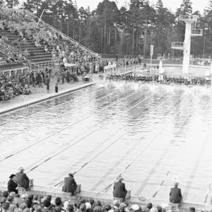 black and white aerial view of a large swimming pool and spectators in filled stands