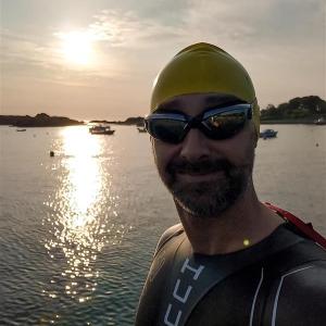 A person in a swim cap, goggles, and wet suit next to a body of water.