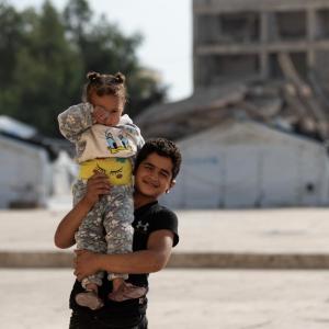 Ahmed *, 8, one of the children who live in the shelter supported by Action Against Hunger, carrying his sister in the back yard of the shelter in Aleppo. 
