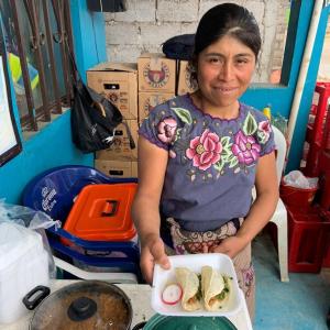 A person handing the photographer a plate of food.