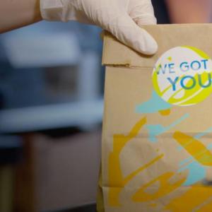 A person wearing gloves hands a paper bag over.