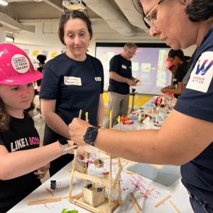 Adult volunteers and children working on building model structures with craft supplies.