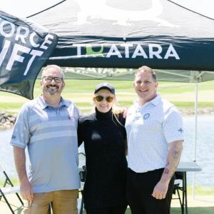 Three people posed in front of a booth "Task Force Uplift" banner above.