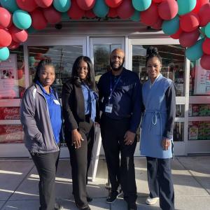Four people posed outside a Walgreens. A balloon arch over the entrance.