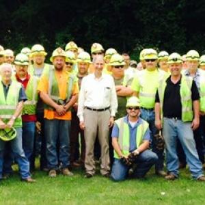 A large team of people posed in a group. Most wearing high-vis vests and safety hats.