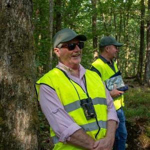 Two smiling people in high-cis vests in a forested area.