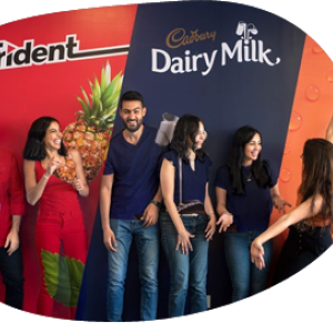 A group of smiling people standing in front of a wall with "Trident" and "Cadbury Dairy Milk" signs.
