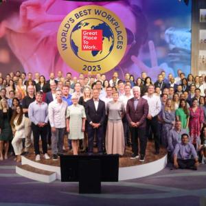 A large group posed on a stage. "World's Best Workplaces" banner above them.