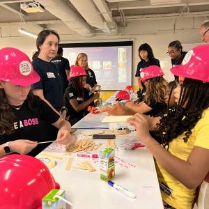 Adult volunteers and children working on building model structures with craft supplies.