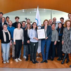 A team of people standing in a round staircase. Two central holding a plaque.