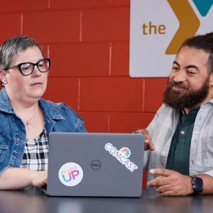 Two people looking at a shared laptop. "The Y" logo on the wall behind them.