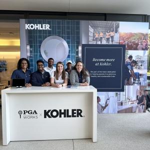 A group posed behind a podium "PGA Works x Kohler" a large display behind them.