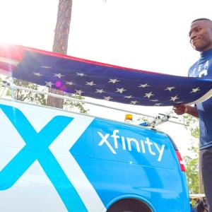 A person folding an american flag. An Xfinity truck to the side.