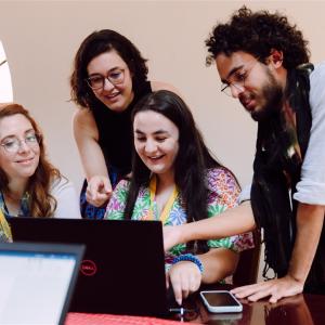 Four people at a desk looking at the same laptop