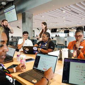 A small group seated at a table, each with a laptop open, talking together.