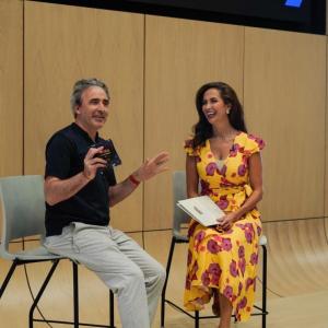 Two people laughing at the front of a room, one with a microphone.