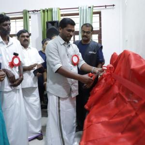 People standing and watching another cut a long red ribbon.