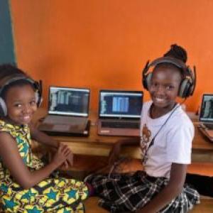 Two smiling children with headphones at a desk with open laptops.