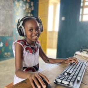 A smiling child with headphones using a computer.