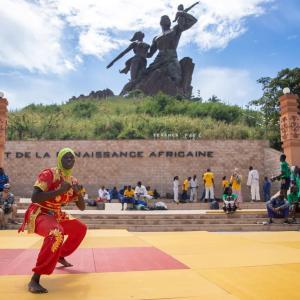 A person in a fighting stance, outside in a park setting, onlookers sit and stand on the sidelines
