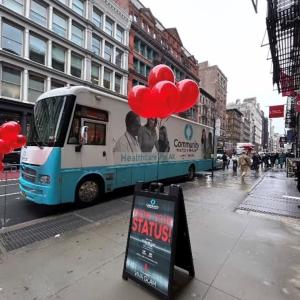 A trailer/bus parked on a street. A sign in front "Know Your Status" with red balloons.