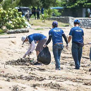 A group of people in matching shirts cleaning a beach.
