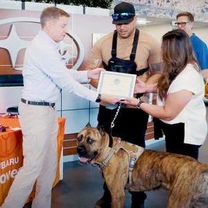 A person handing over a certificate to a couple who are stood with a service dog 