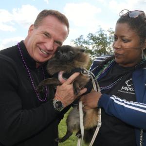 Two people holding a small dog between them outside.