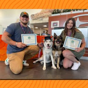 Two people with their dogs and certificates of graduation.