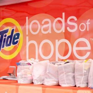tent with banner "Tide loads of Hope". Bags of laundry on a table.