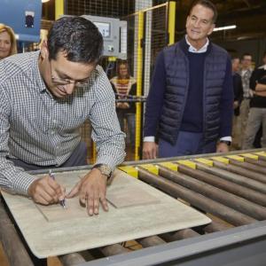 Matthew Sanchez signing the back of a tile on a conveyor line.