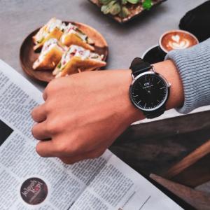 a hand with a watch, a newspaper and food on the table