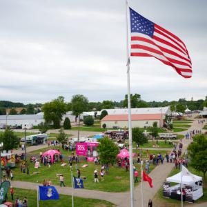 aerial view of a campground, an American flag on a tall pole, vendor booth tents and out buildings on the grounds.