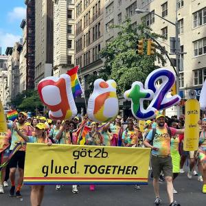 People marching down a street with balloons and a banner "got2b glued together".