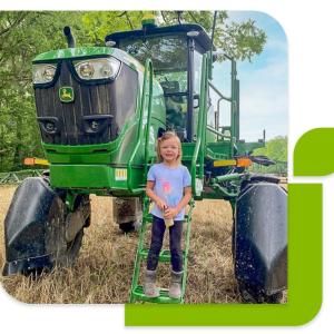 A child on the steps up to a green tractor.