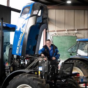 A mechanic standing next to a farm tractor with an open hood.