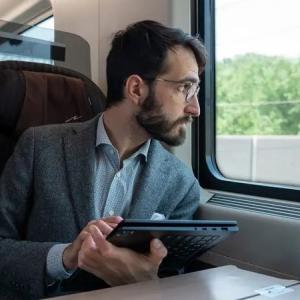 Ruggero Rollini looking out a train window, holding an open tablet.