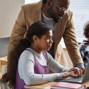 A teacher helping a student in a classroom, using a laptop