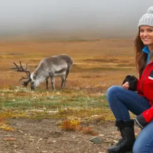 A person crouched on an open plain, a caribou in the distance
