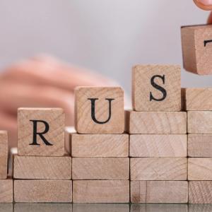 A person stacking wood blocks, the top ones spell out trust.