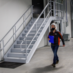 A person walking through a long hallway. A staircase to their right.